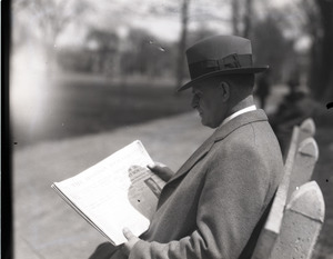 Clarence E. Jacobson, seated on a park bench, reading a copy of the Boston Herald