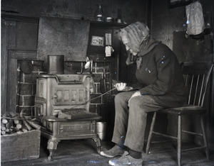 Reuben Austin Snow, the cross-dressing hermit of Cape Cod, stoking a fire in a wood stove