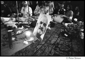 View of stage with Ram Dass singing at the Winterland Ballroom gathering, with portrait of Neem Karoli Baba in the foreground