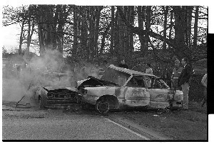 Fireman playing with a golf club at the scene of a burnt-out car in which the occupant had been killed