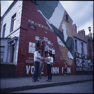 Gerry Adams, President of Sinn Fein, posing in front of a Sinn Fein republican wall mural on the Falls Road, Belfast, and with Mairead Corrigan of the Peace People in front of the mural