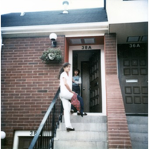 Two young women on the front steps and at the open front door of a Villa Victoria row house.