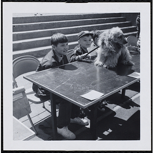 Two boys sitting at a table with a dog in a Boys' Club Pet Show
