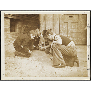 A Group of boys kneeling in a circle outside and playing a game