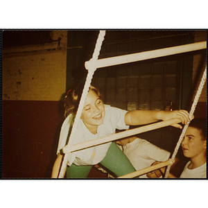 A girl climbs a rope ladder in a gymnasium