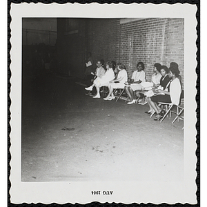 Participants' families sit in chairs in front of a wall during a Boys' Club Little Sister Contest