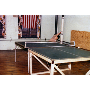 Boy playing a game of ping-pong leans over to the right to successfully make an overhead shot