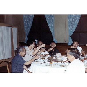 Men sit around a dinner table and raise their glasses for a toast