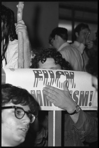 Paul Krassner hiding behind a sign reading 'Fuck Communism'