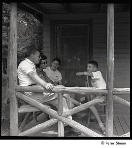 Camp Arcadia: camper talking with adults, seated on a cabin porch