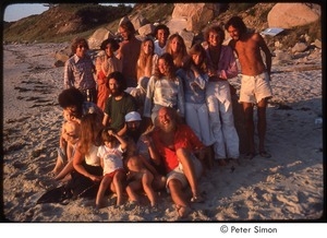 Ram Dass posing on the beach with a group including Ronni Simon (hand on RD's knee) and Mirabai Bush (2nd from left, seated), Daniel Goleman in plaid shirt back left