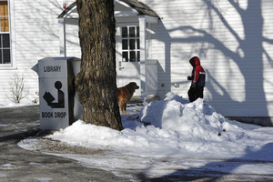 Child and golden retriever playing in snow in front of new New Salem Public Library