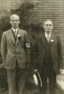 Two alumn pose in front of a brick wall, one from the class of 1912, and one from the class of 1887