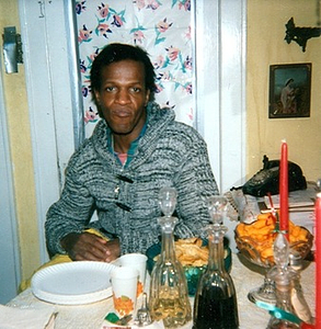 A Photograph of Marsha P. Johnson Sitting at the Kitchen Table Wearing a Gray Sweater
