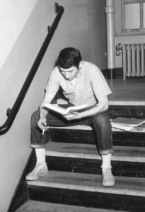 A Suffolk University students sits in a stairwell, studying and smoking a cigarette