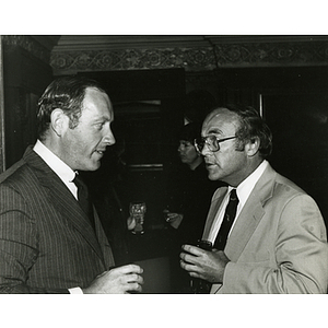 Two men stand and converse with drinks in their hands at a Boys' Club meeting