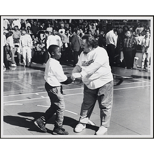 Boston radio personality Andy Moes shakes hands with a boy on a basketball court, while the spectators look on, at a fund-raising event held by the Boys and Girls Clubs of Boston and Boston Celtics