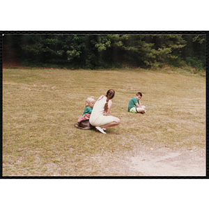 A boy and a girl in green sitting apart in a field while a woman talks to the girl during a Boys & Girls Club event