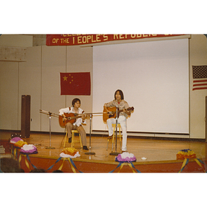 Two Chinese men play guitars onstage in the Josiah Quincy School auditorium at the 30th anniversary celebration of the People's Republic of China