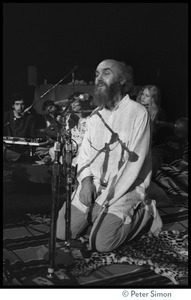 Ram Dass kneeling at the microphone, addressing the audience at the Winterland Ballroom during his 'marathon'