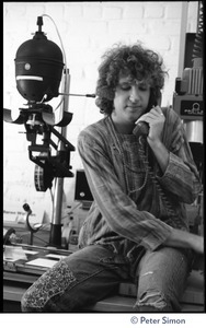 Peter Simon seated in a darkroom next to an enlarger, talking on the telephone