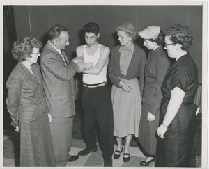Four women and one man examining a young man's injured arm