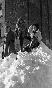 Three women posing atop large snowpile