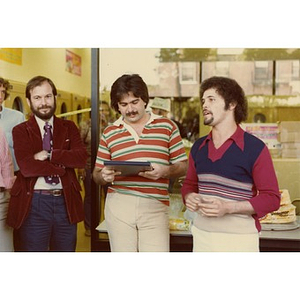 Jorge Hernandez standing with two other men in front of a laundromat, one of whom appears to be addressing the crowd.