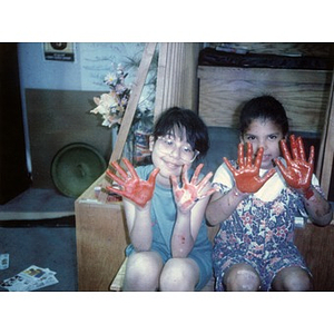 Two little girls display hands covered in red paint.