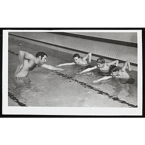 A man offers swimming lessons to three boys in a pool
