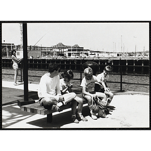 Three children waiting on a bench next to their counselor at the Charlestown Navy Yard