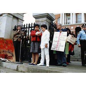 Two children speaking into a microphone from the steps of the Massachusetts State House at a rally for bilingual education in schools