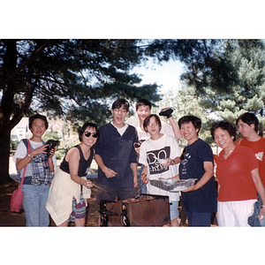 Men and women, including Suzanne Lee, stand around a grill during a Chinese Progressive Association picnic