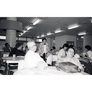 Chinese Progressive Association members sit at tables while a woman speaks to them