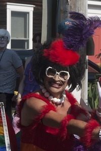 Parade marcher in a feathery costume on a scooter, grinning : Provincetown Carnival parade