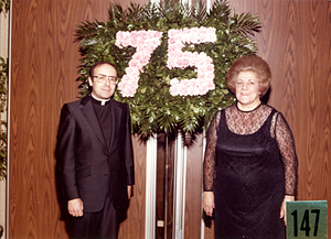 Fr. Eusebio Silva and Gladys Picanso in front of 75th anniversary banner
