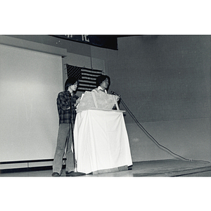 Two Chinese men stand at the podium onstage in the Josiah Quincy School auditorium at an event about the normalization of U.S. and China relations