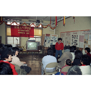 Seated guests watch TV at an International Women's Day event