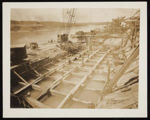 A view of steam shovels and men standing on timber frames during construction of the Cape Cod Canal.