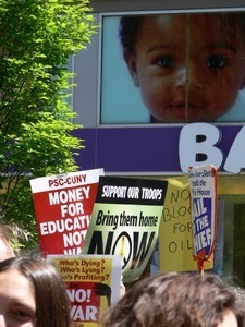 Antiwar marchers in the streets of New York with signs and banners opposing the war in Iraq, passing by a Toys R Us store with images of babies