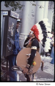 MUSE concert and rally: man in Native American ceremonial dress talking on a payphone