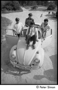 Four unidentified men posed on a Volkswagen Beetle, with a dog in the foreground