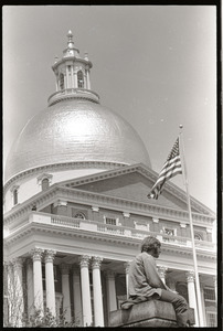 Demonstration at State House against the killings at Kent State: protester seated on stone pillar, capitol dome in background