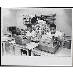 A teenage boy tutors two other teenage boys using typewriters