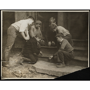 A Group of six boys sitting on some steps outside and playing a dice game
