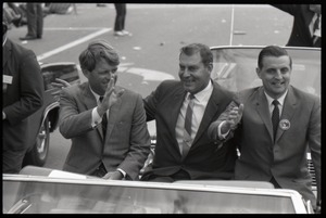 Robert F. Kennedy (left) and Walter Mondale (right) riding in an open car at the Turkey Day parade while stumping for Democratic candidates in the northern Midwest