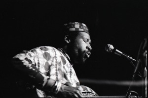 Taj Mahal in concert at Northfield, Mass.: Taj Mahal seated, playing steel guitar (blurred)