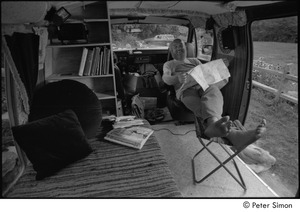 Ram Dass in his van: Ram Dass with his feet up, smiling and holding a map