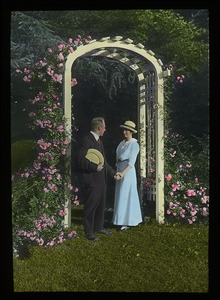 Couple under flower-covered arbor: probably at the original entrance to the Rhododendron Garden on the Massachusetts Agricultural College