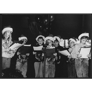 Group of children wearing Santa Claus holding up folders and singing